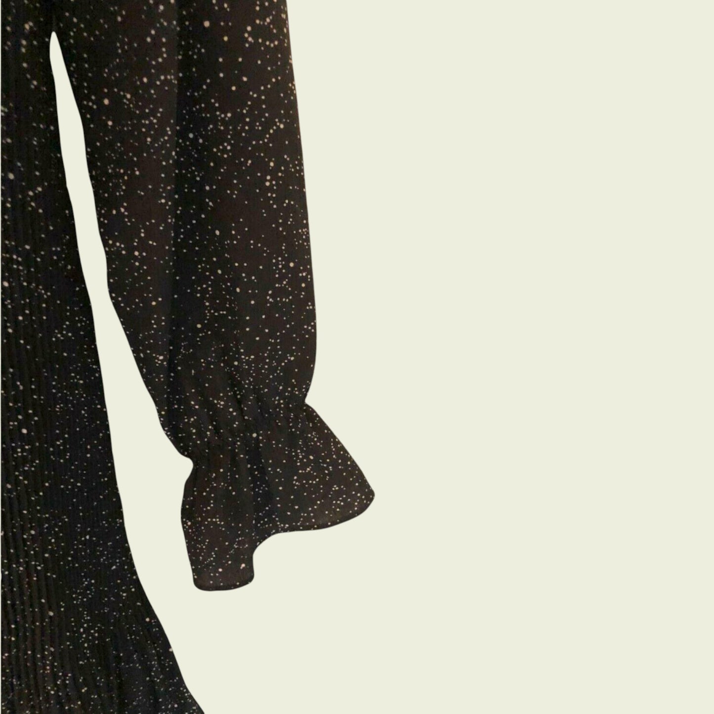 Sleeve of black and white polka dot pleated dress on beige background