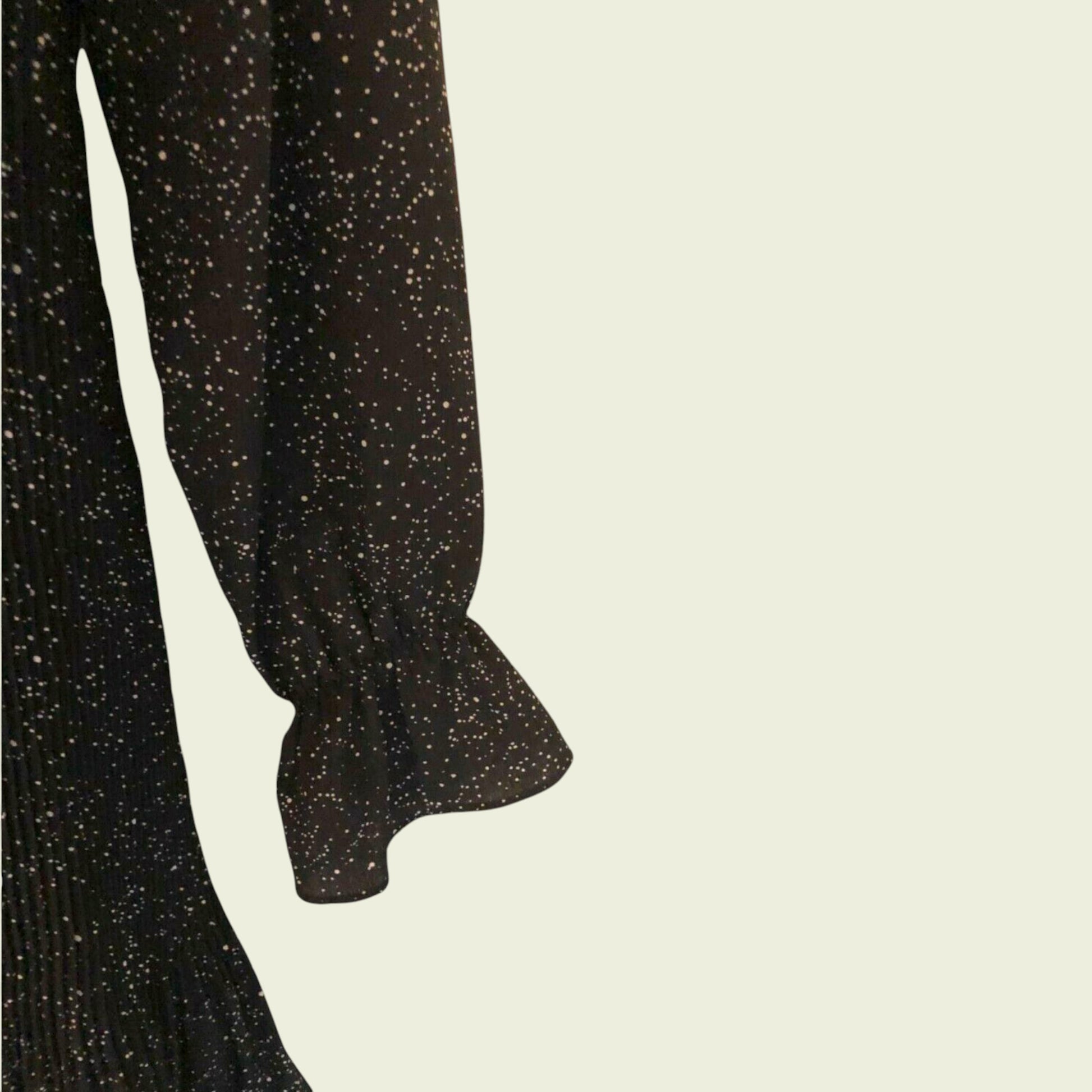Sleeve of black and white polka dot pleated dress on beige background