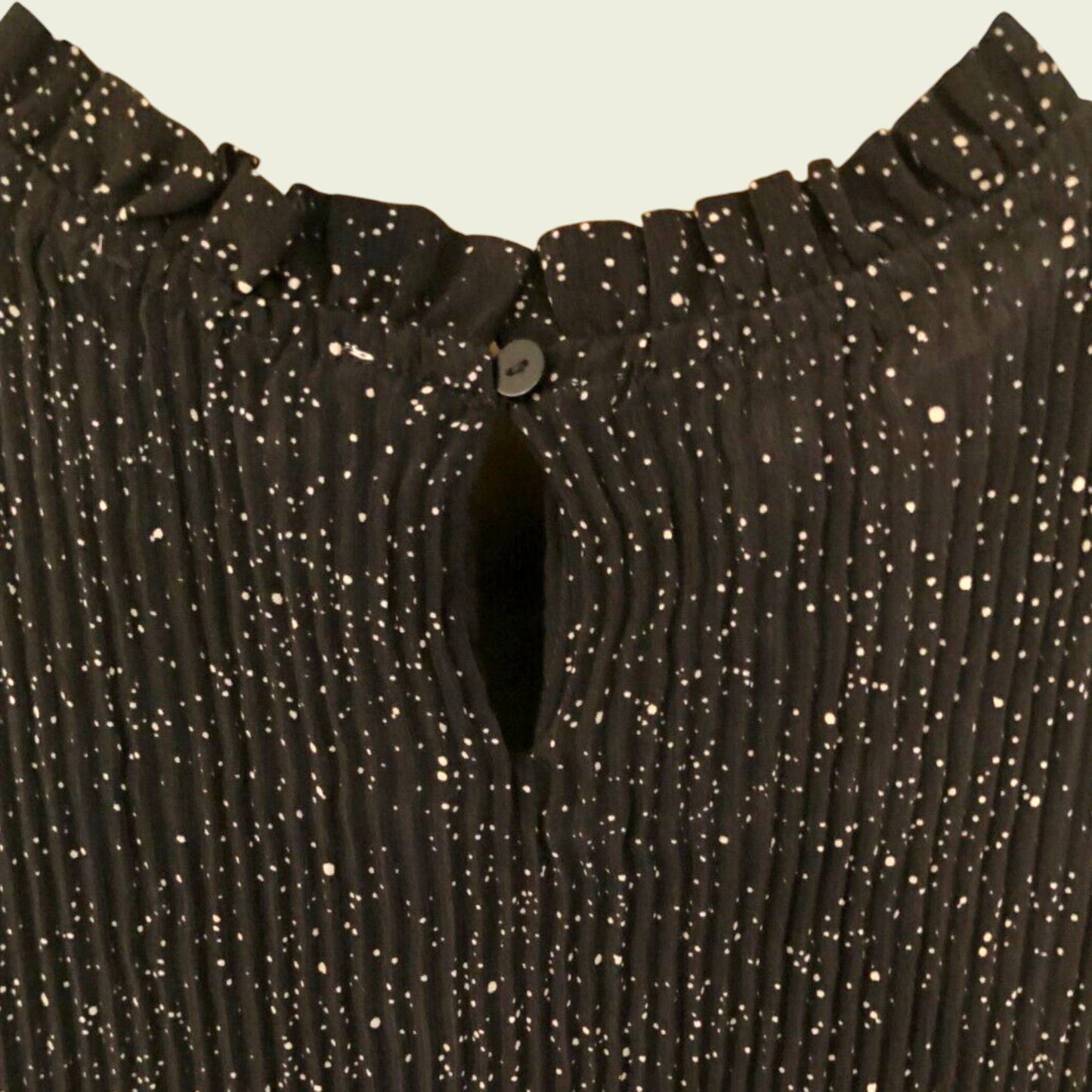 Button closure of black and white polka dot pleated dress on beige background