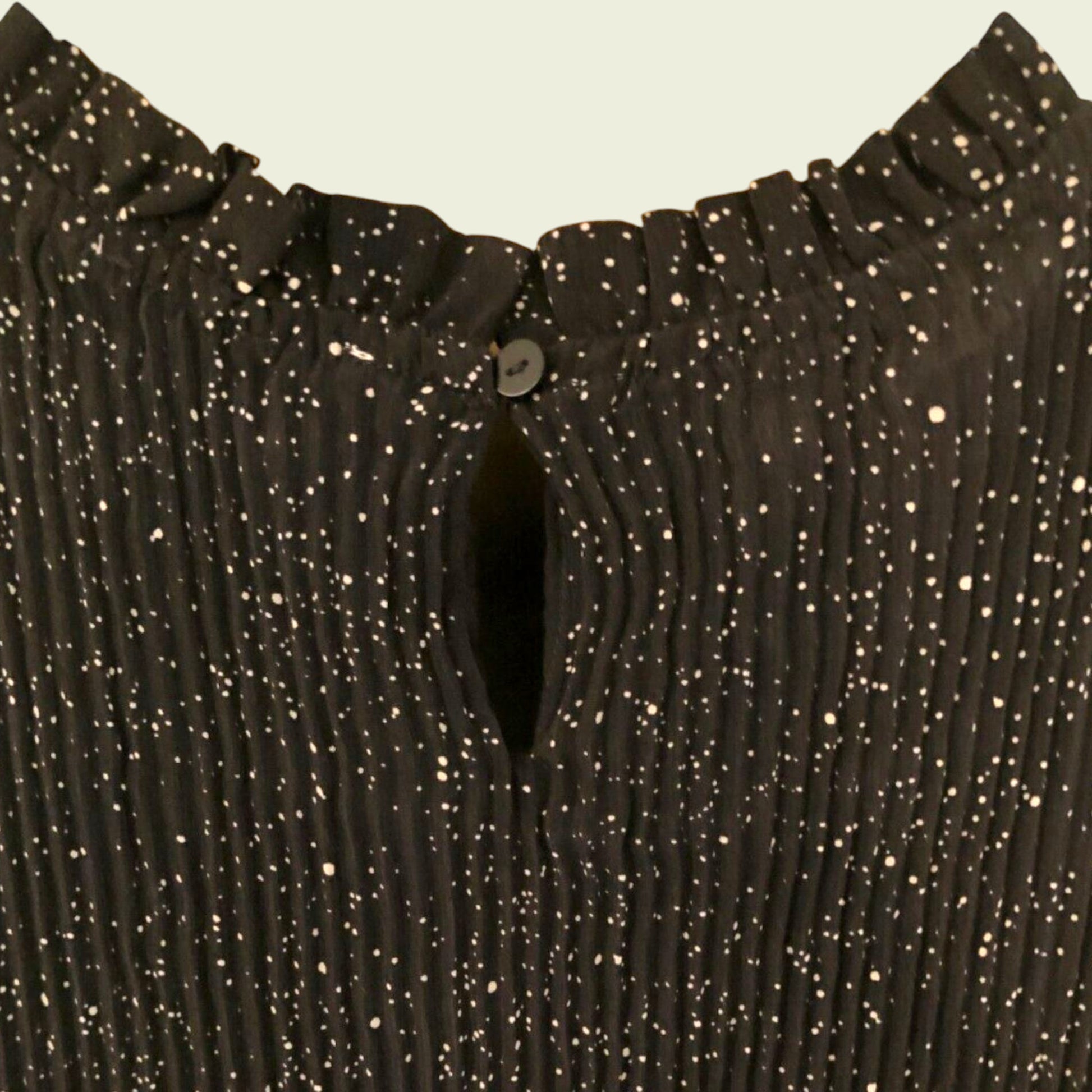 Button closure of black and white polka dot pleated dress on beige background