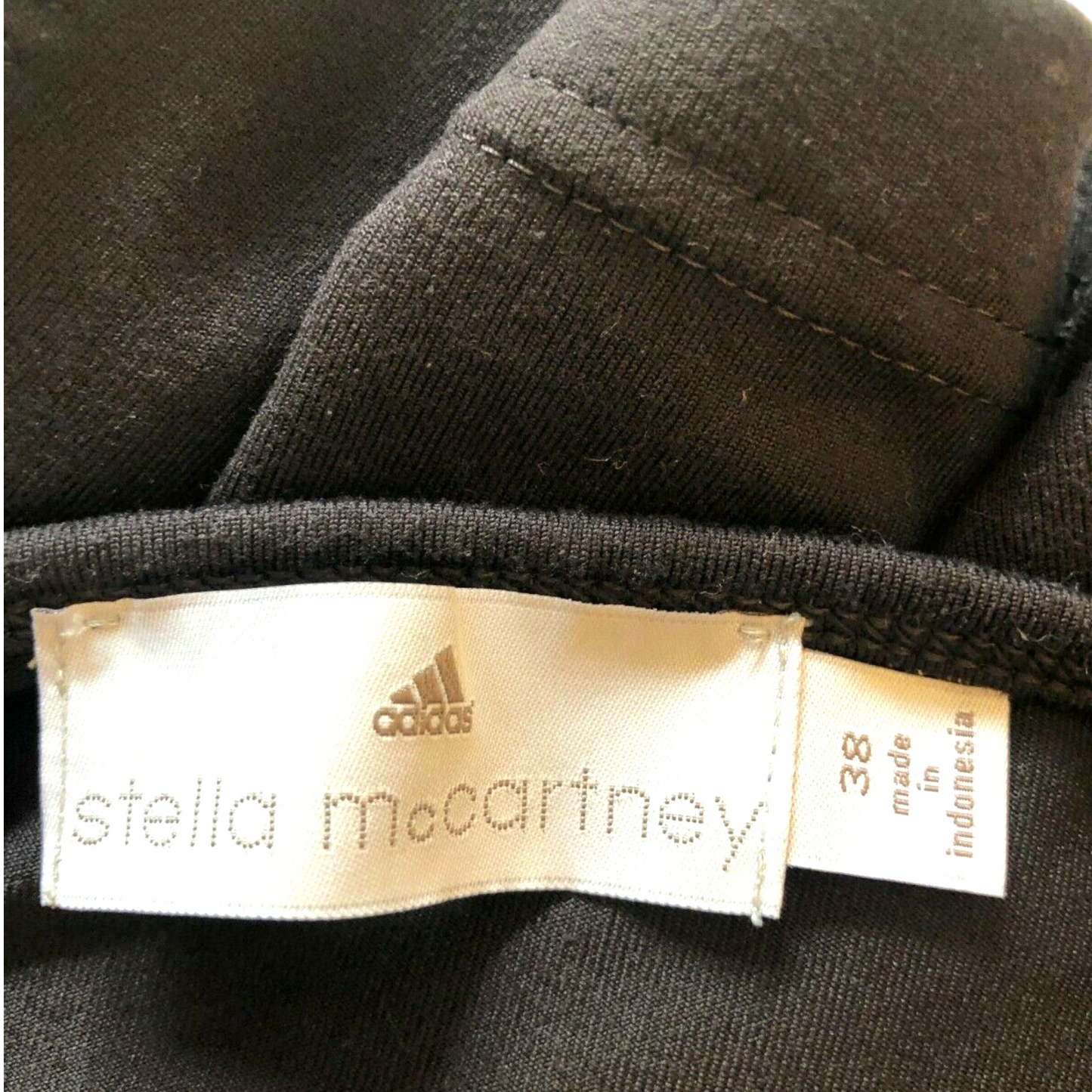 Close-up of a label on a dark brown garment featuring Adidas and Stella McCartney logos.