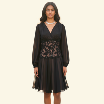 A woman modeling a black long-sleeve midi dress with a sheer lace waist panel, photographed against a plain light beige studio background.