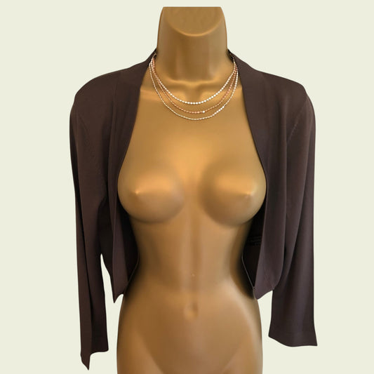 Mannequin wearing a brown shrug with layered necklaces on a beige background