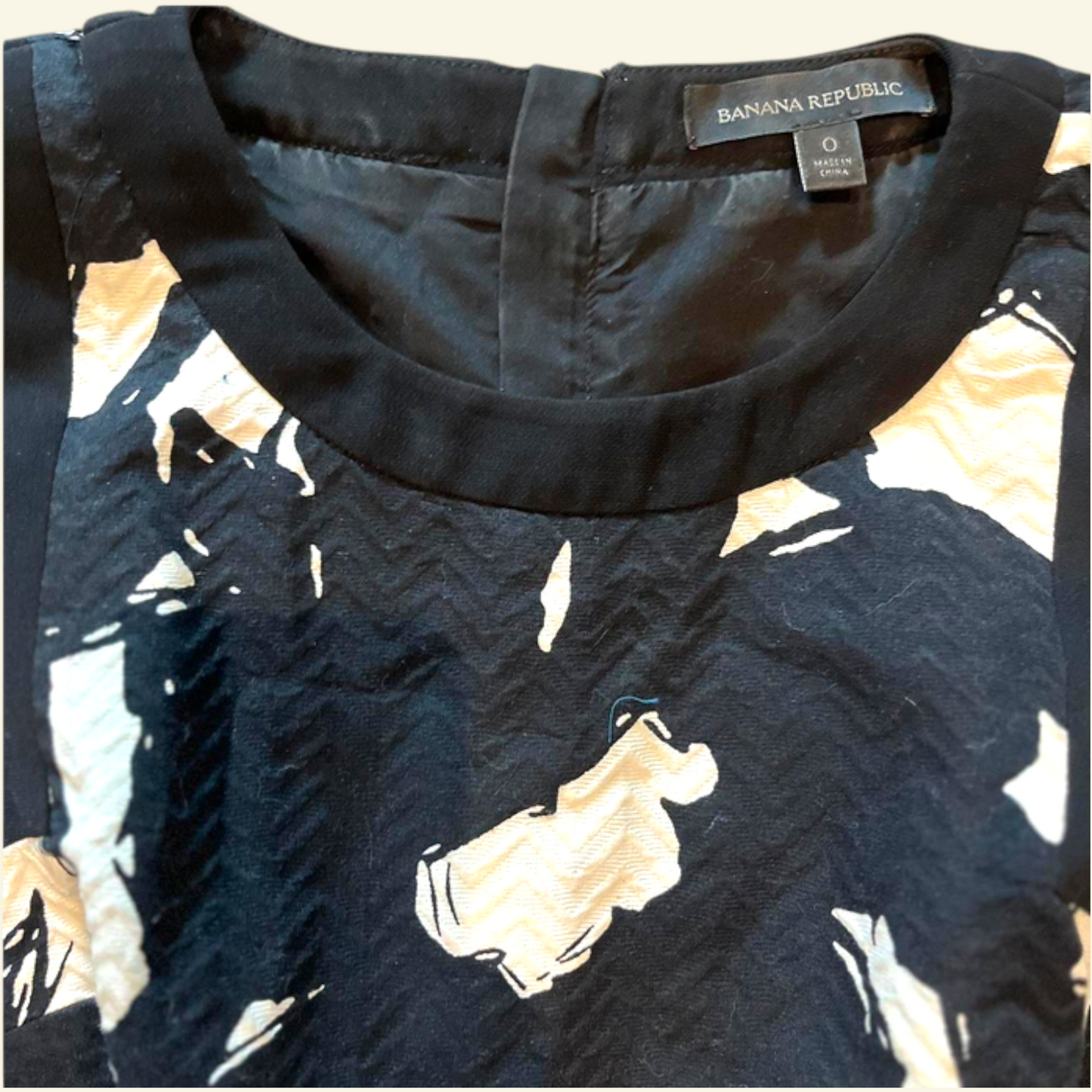 Close-up of a Banana Republic women's top showing the inner neckline with a black satin-like trim and a black fabric printed with abstract beige and cream shapes.