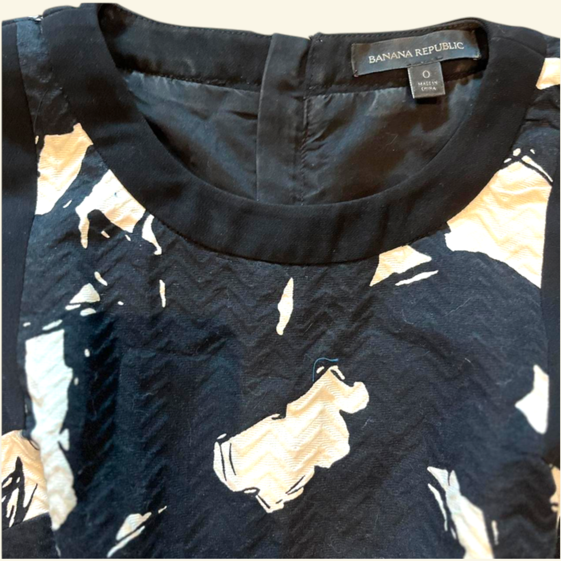 Close-up of a Banana Republic women's top showing the inner neckline with a black satin-like trim and a black fabric printed with abstract beige and cream shapes.