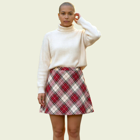 Person wearing a white sweater and red plaid skirt on a beige background