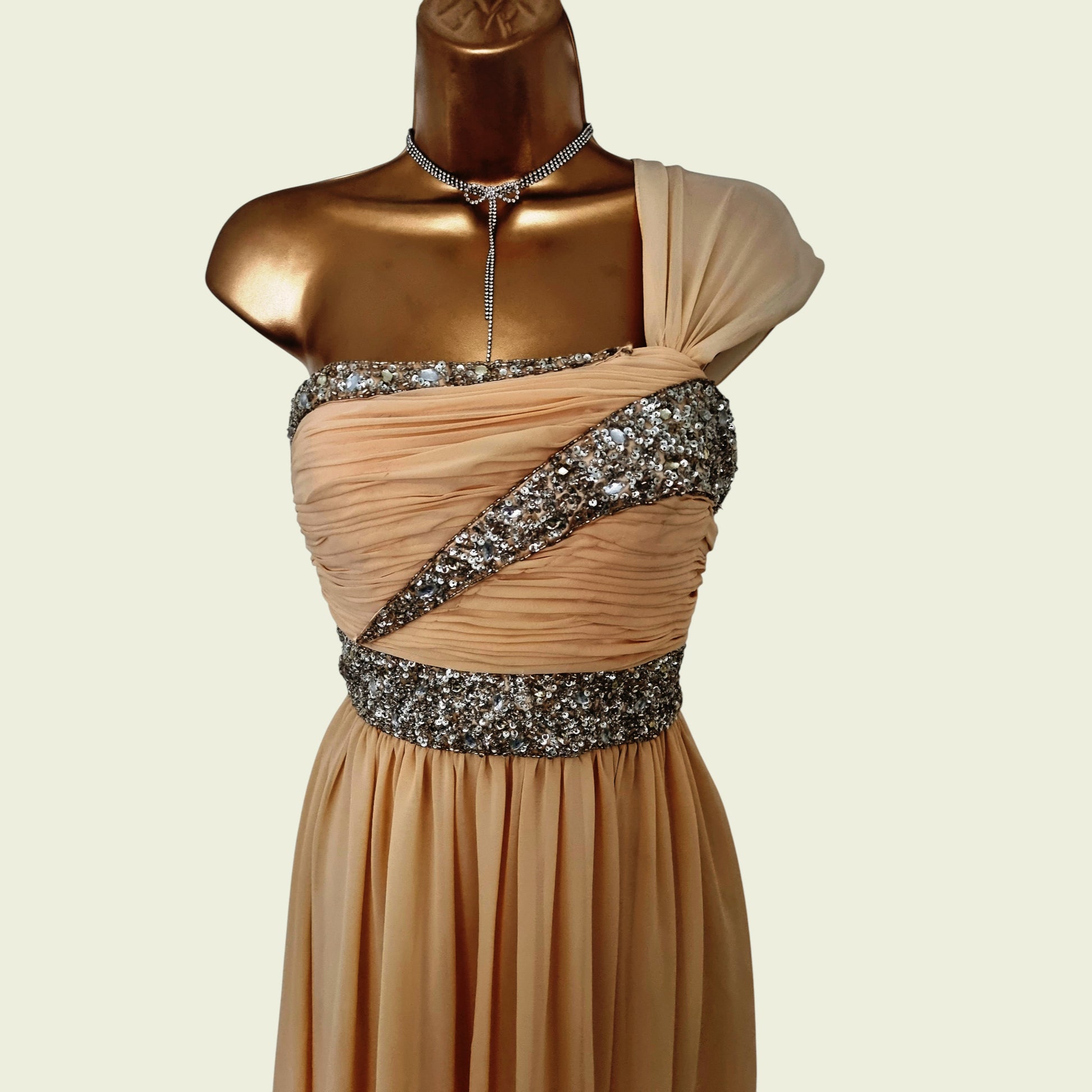 Beige evening gown with silver embellishments on a mannequin against a beige background