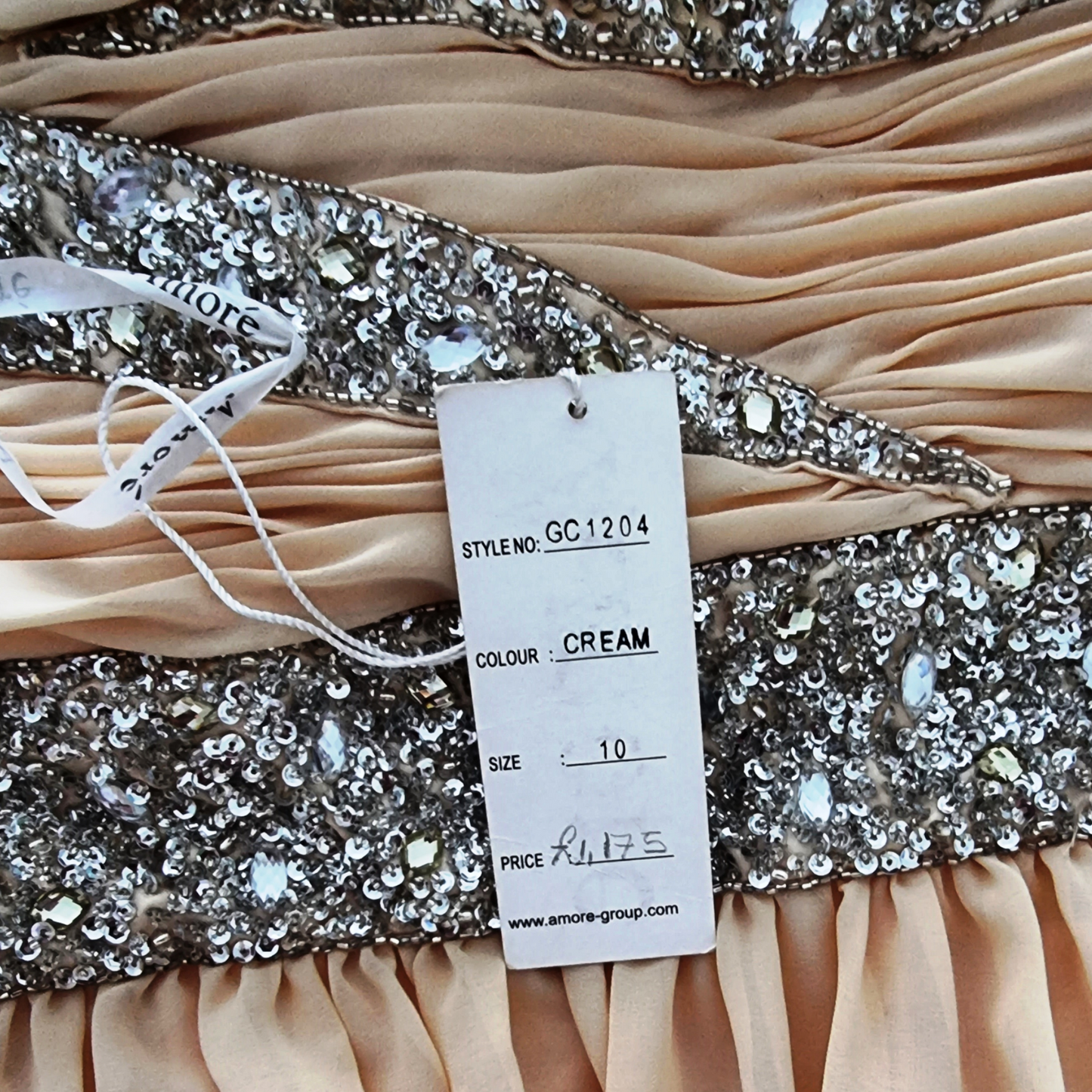 Close-up of a cream dress with a sequined belt and a tag displaying details.