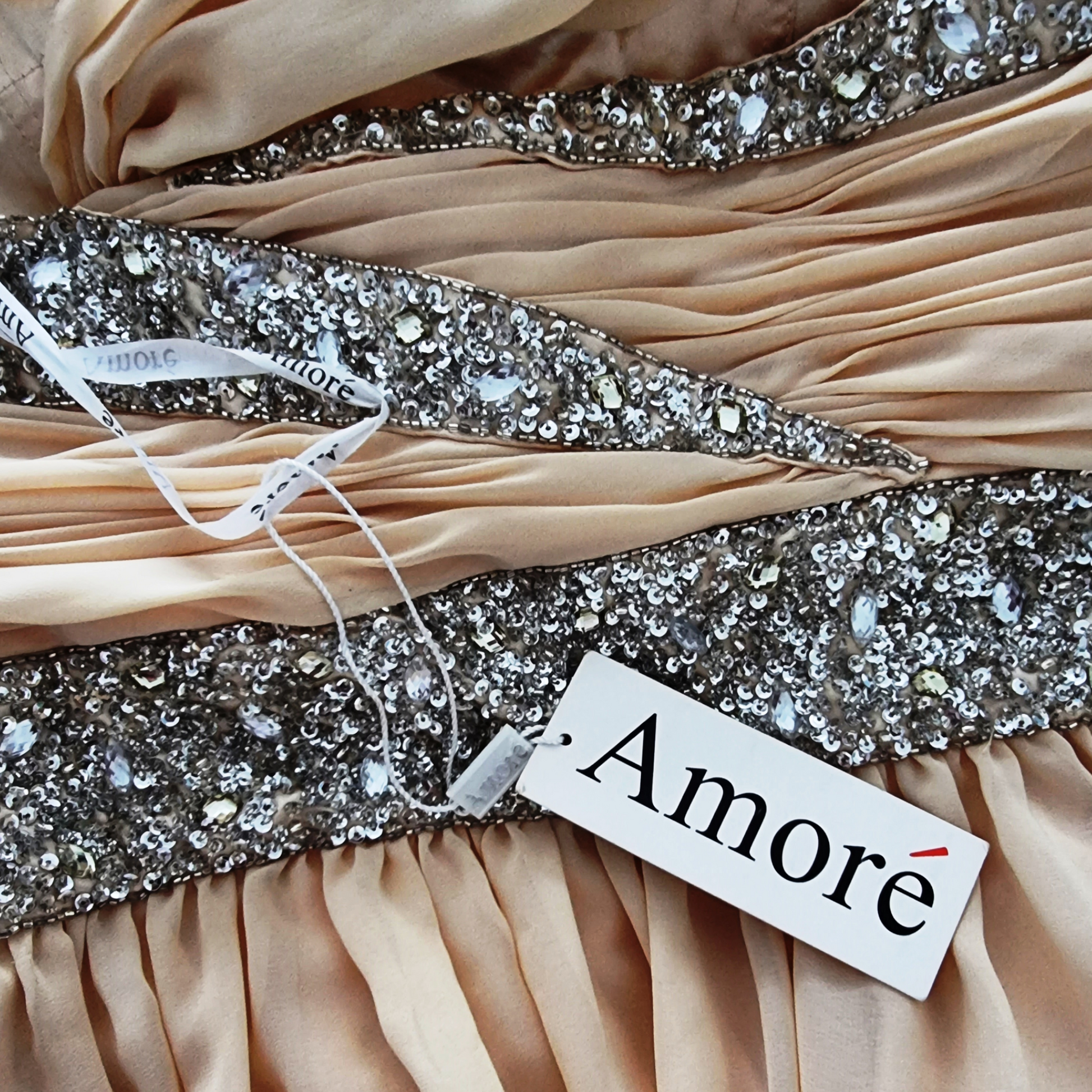 Close-up of a beige dress with a sparkling belt and 'Amore' label.
