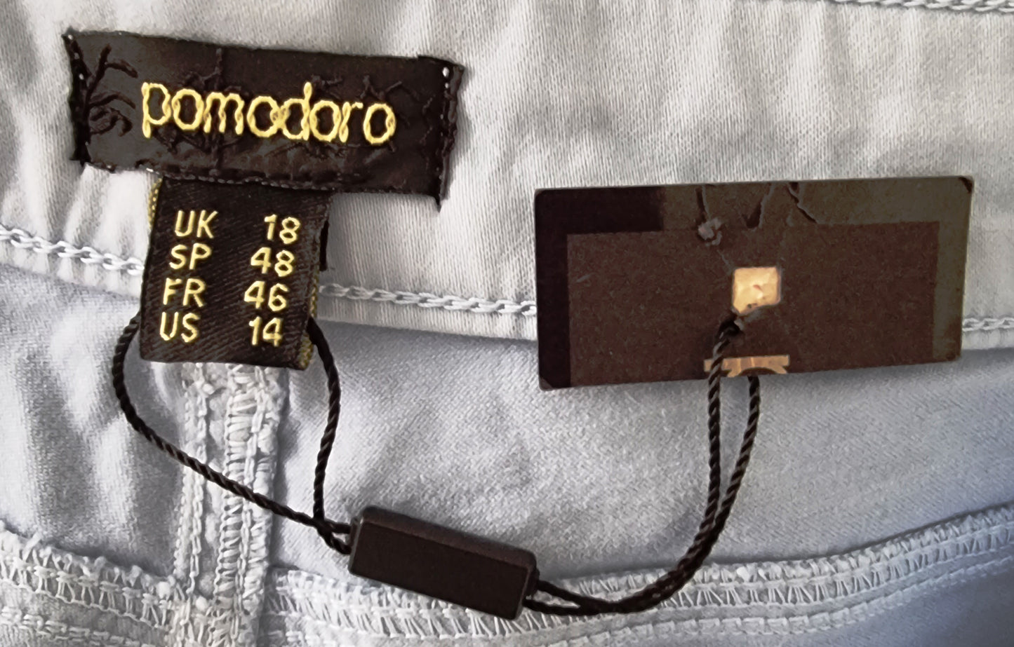 Close-up of clothing tags with brand name 'pomodoro' on a light fabric background