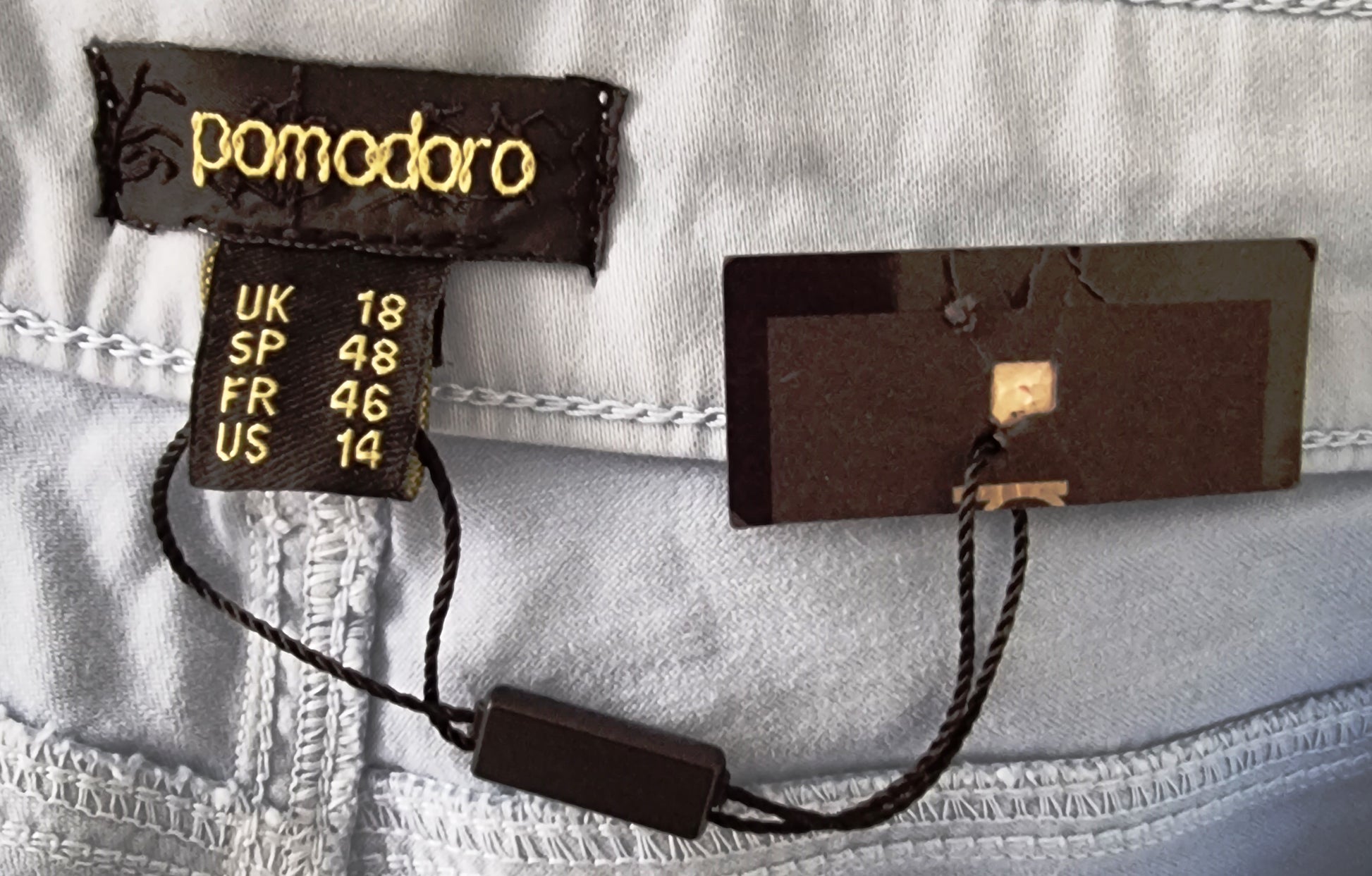 Close-up of clothing tags with brand name 'pomodoro' on a light fabric background