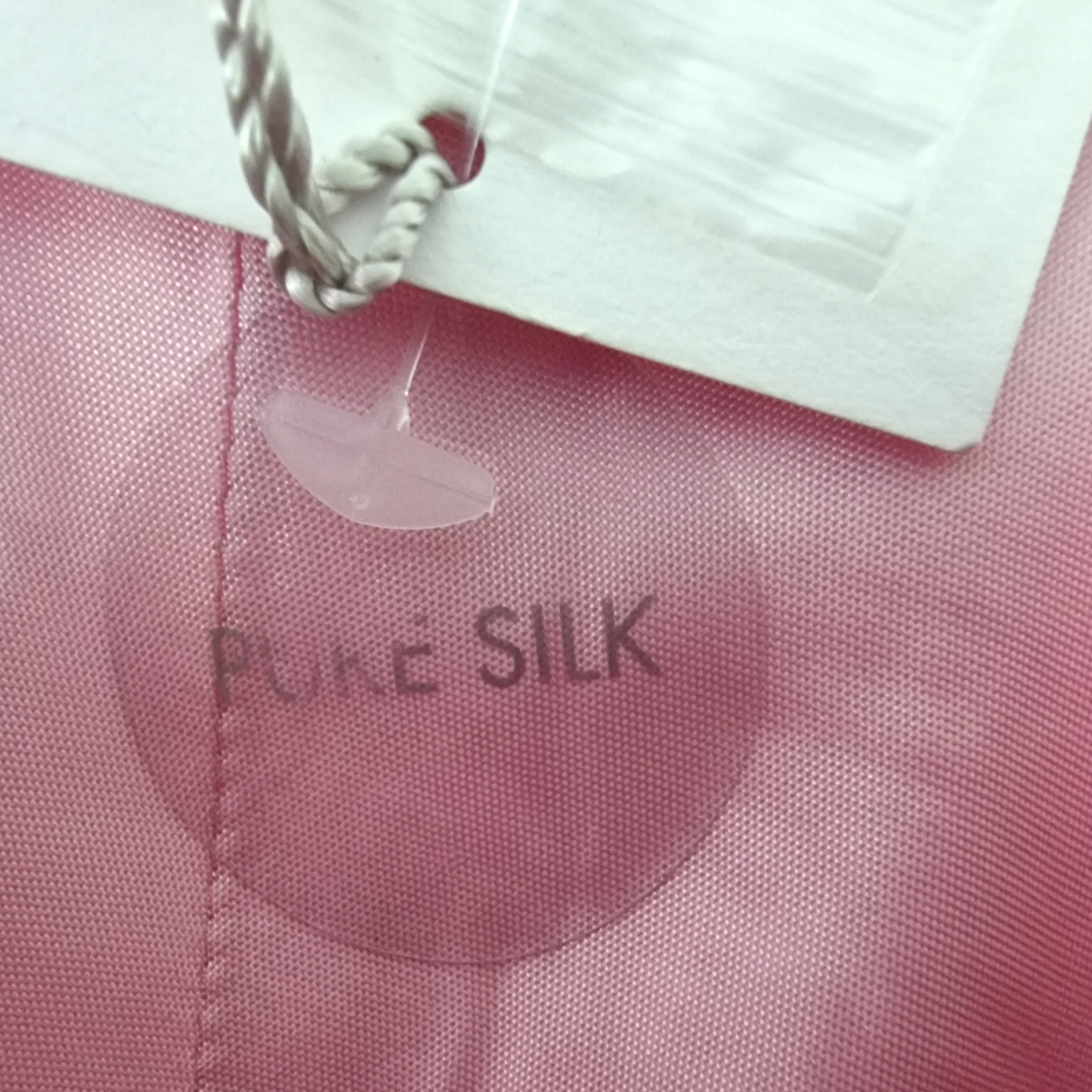 Pink fabric with 'Pure Silk' label and a silver pendant.