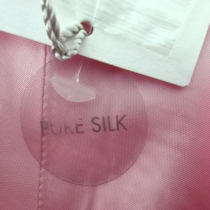 Pink fabric with 'Pure Silk' label and a silver pendant.
