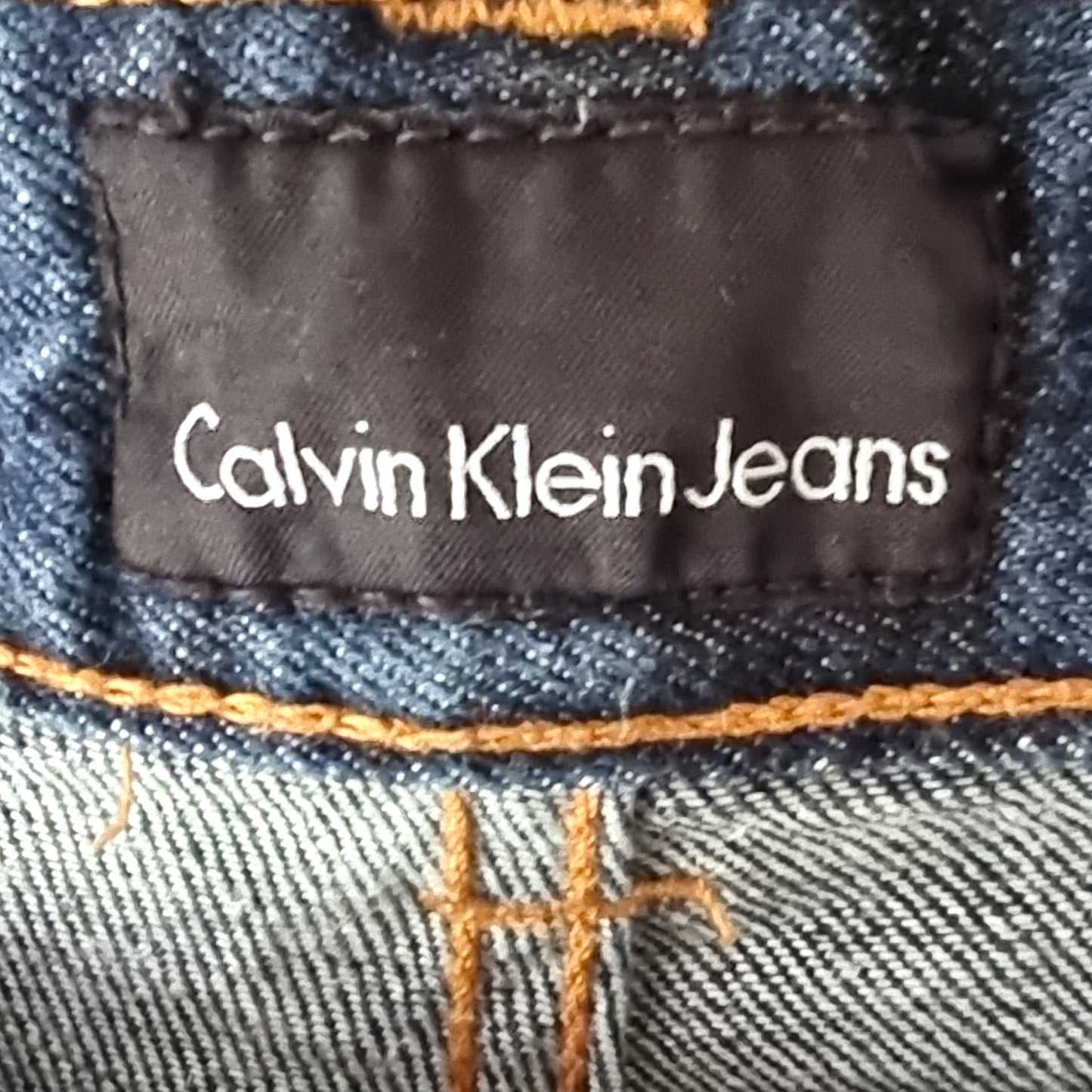 Calvin Klein Jeans label on a denim fabric with orange stitching.
