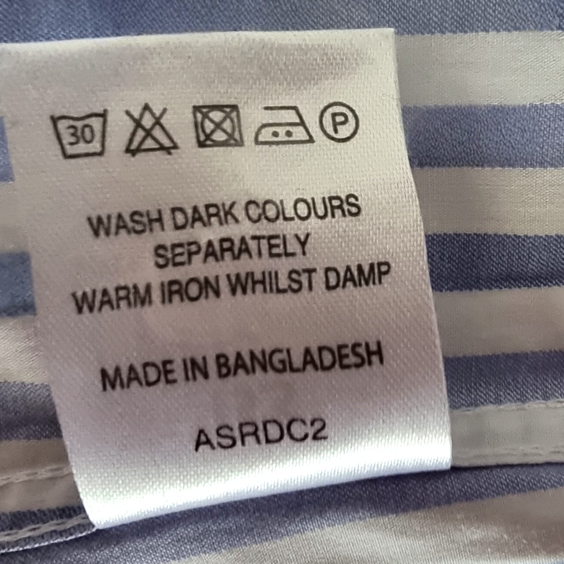Clothing label with washing instructions and product details on a striped fabric background