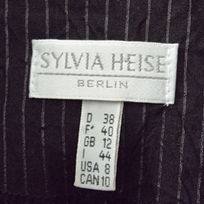 Label with 'SYLVIA HEISE BERLIN' on a dark pinstripe fabric background