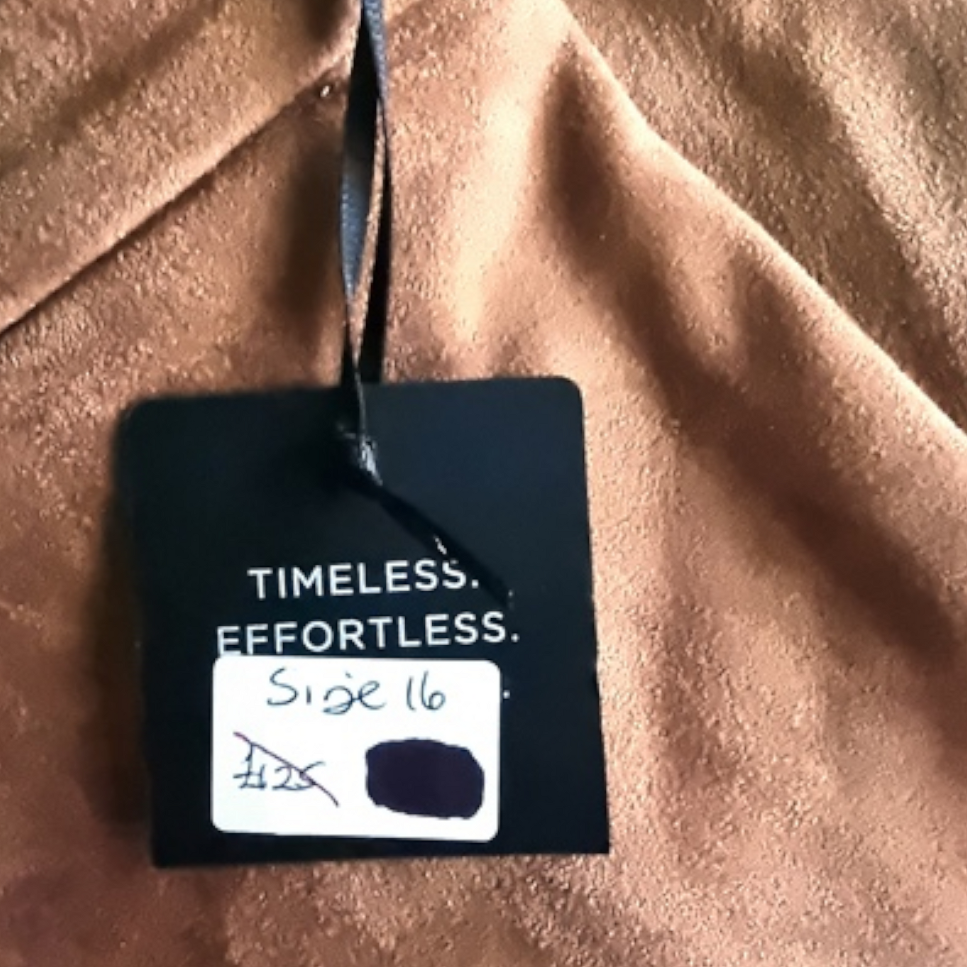 Clothing tag on a brown fabric background with text 'Timeless. Effortless.'