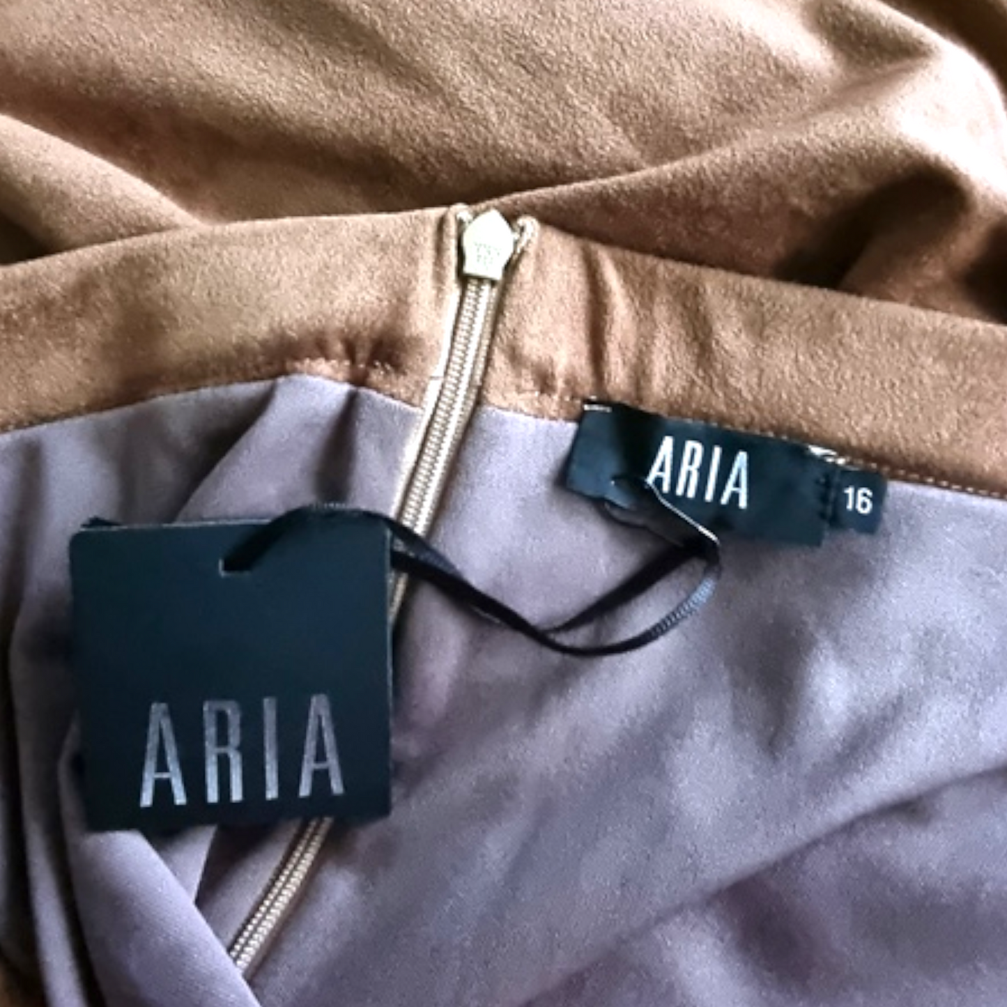 Close-up of a skirt with 'ARIA' branding on a brown and gray fabric background.