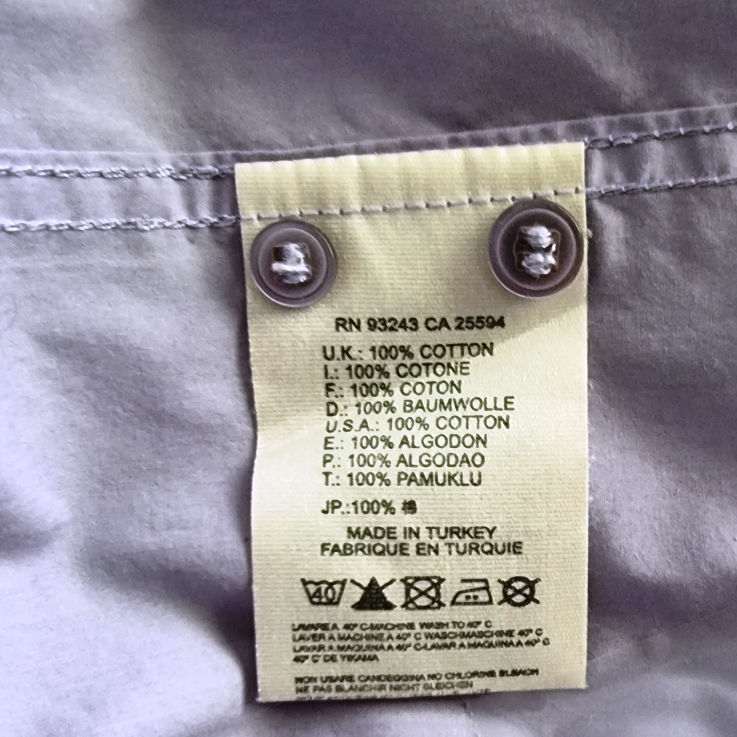 Garment label with fabric content and care instructions on lilac background