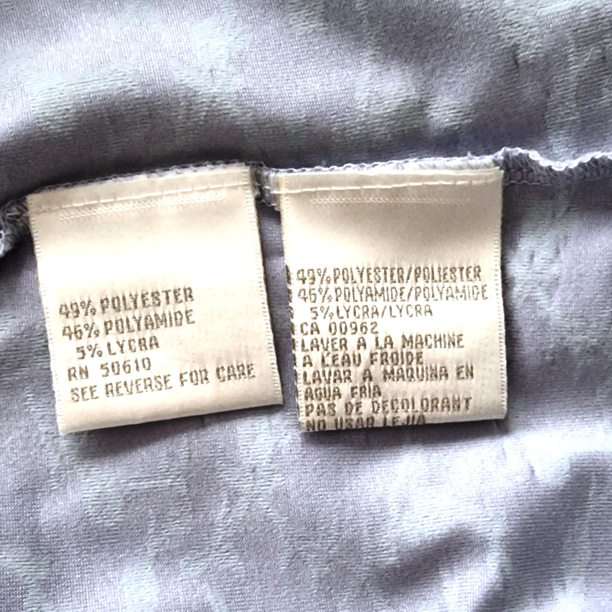 Clothing labels with fabric composition and care instructions on a gray fabric background