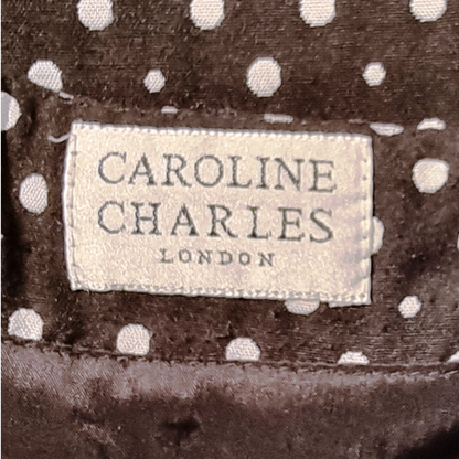 Label with 'Caroline Charles London' on a black fabric background with white polka dots.