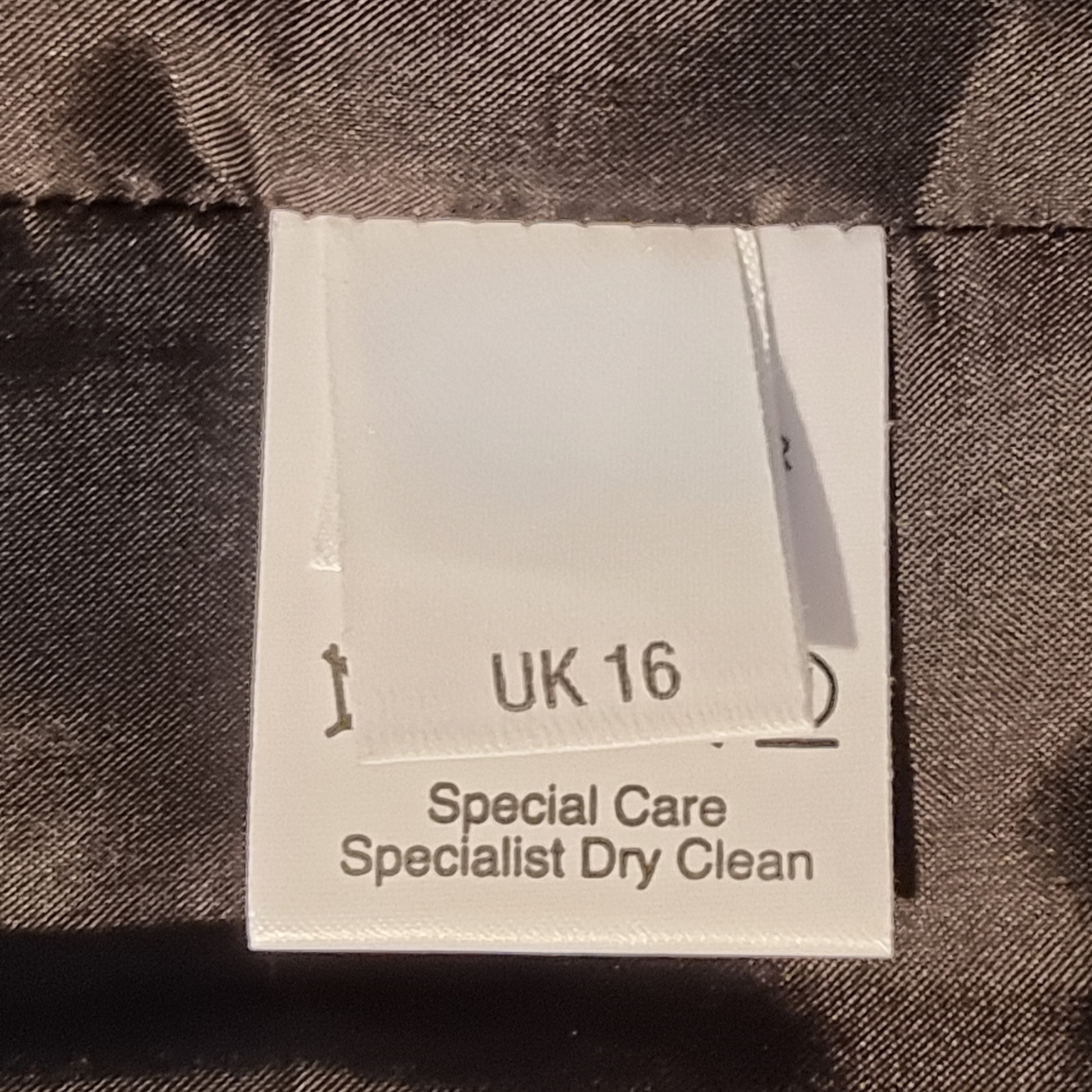 Fabric tag with size 'UK 16' and care instructions on a textured fabric background