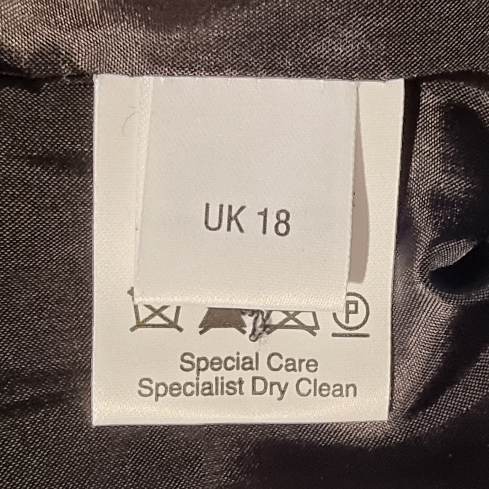Clothing label with size 'UK 18' and care instructions on a dark fabric background