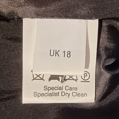 Clothing label with size 'UK 18' and care instructions on a dark fabric background