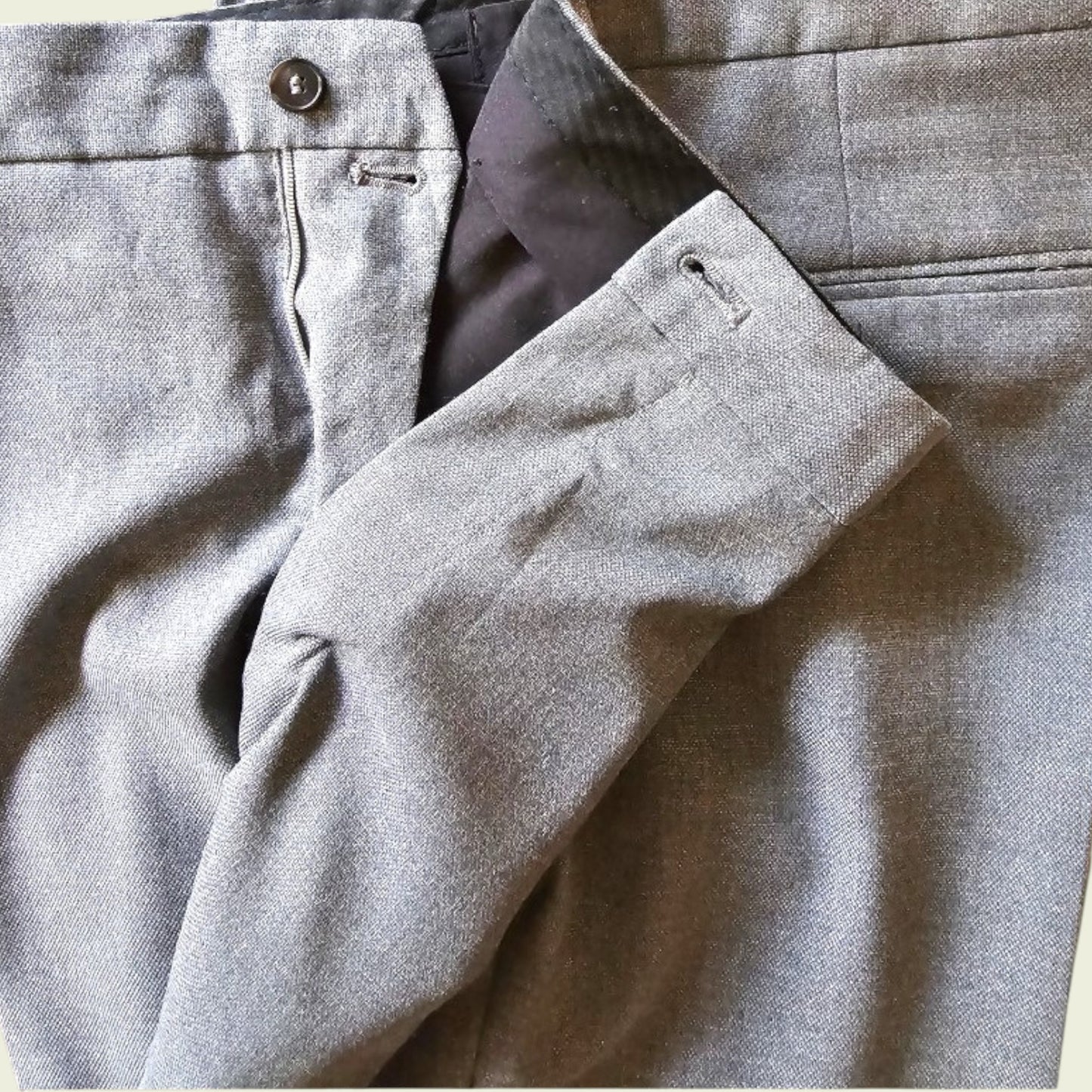 Close-up of gray pants with a button and pleated texture.