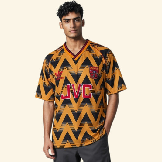 A man modeling a vintage-style football jersey with a bold yellow and black chevron pattern, featuring red JVC lettering on the chest and club crests.