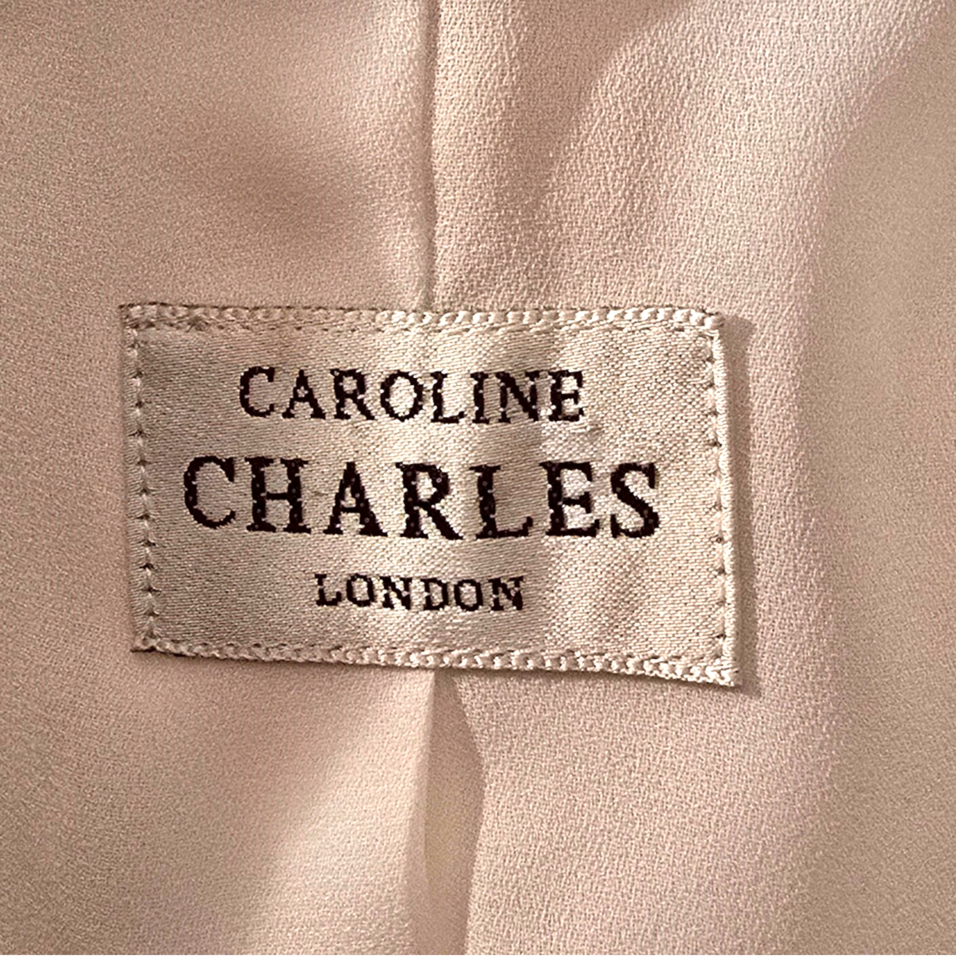 Label with 'Caroline Charles London' text on a beige fabric background