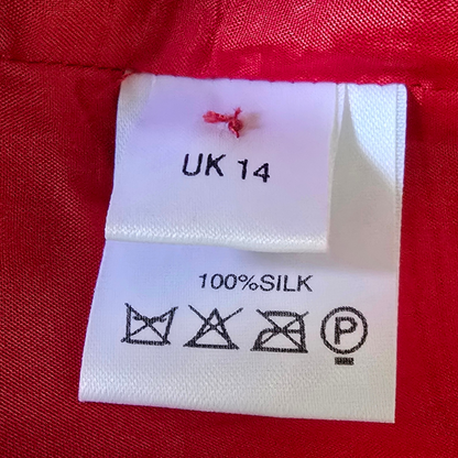 Fabric label with size 'UK 14' and material '100% Silk' on a red fabric background.
