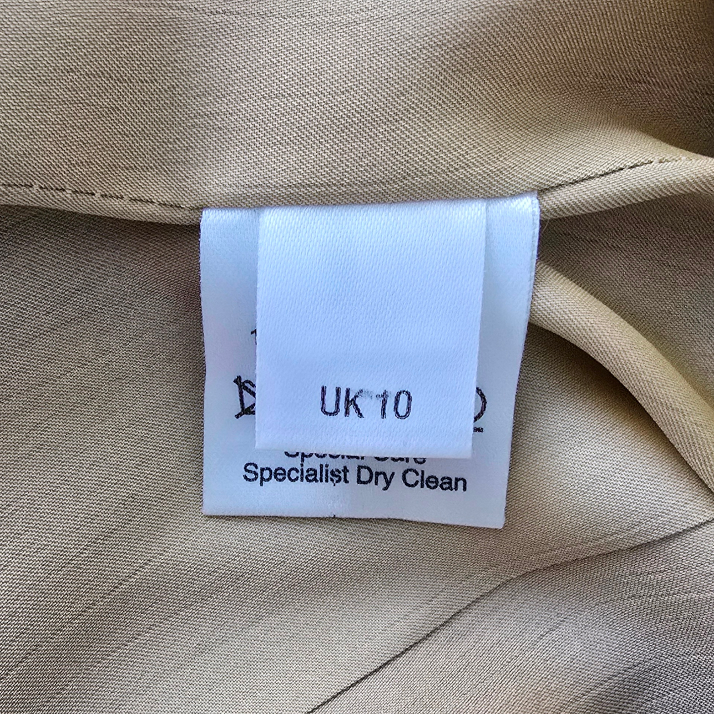 Clothing tag on beige fabric with size 'UK 10' and dry cleaning instructions.