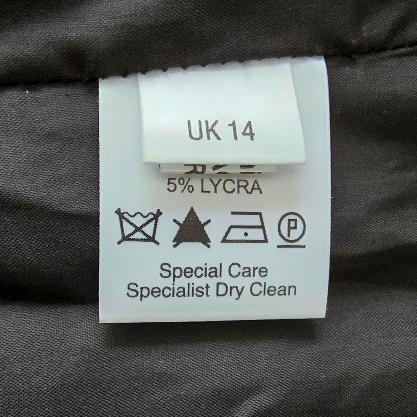 Clothing label with size 'UK 14' and care instructions on a dark fabric background