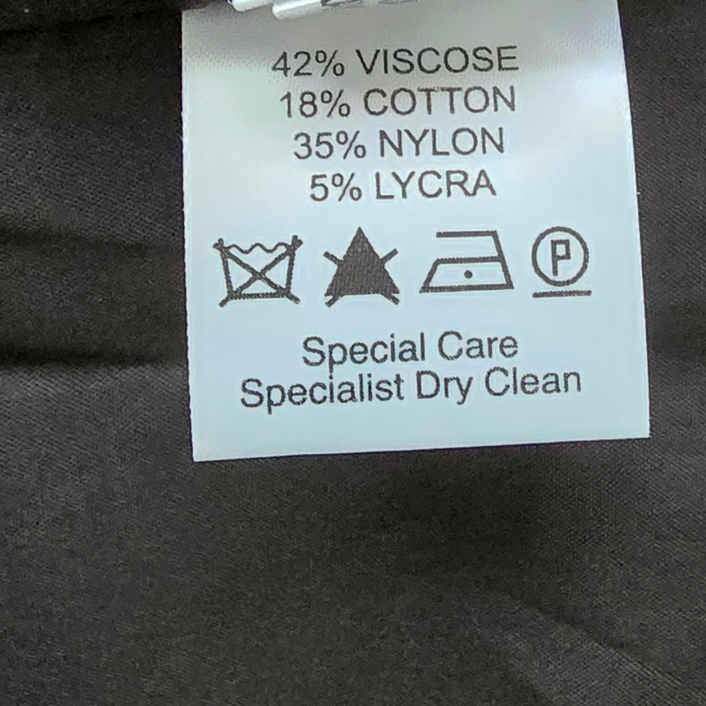 Clothing label with fabric composition and care instructions on a dark fabric background