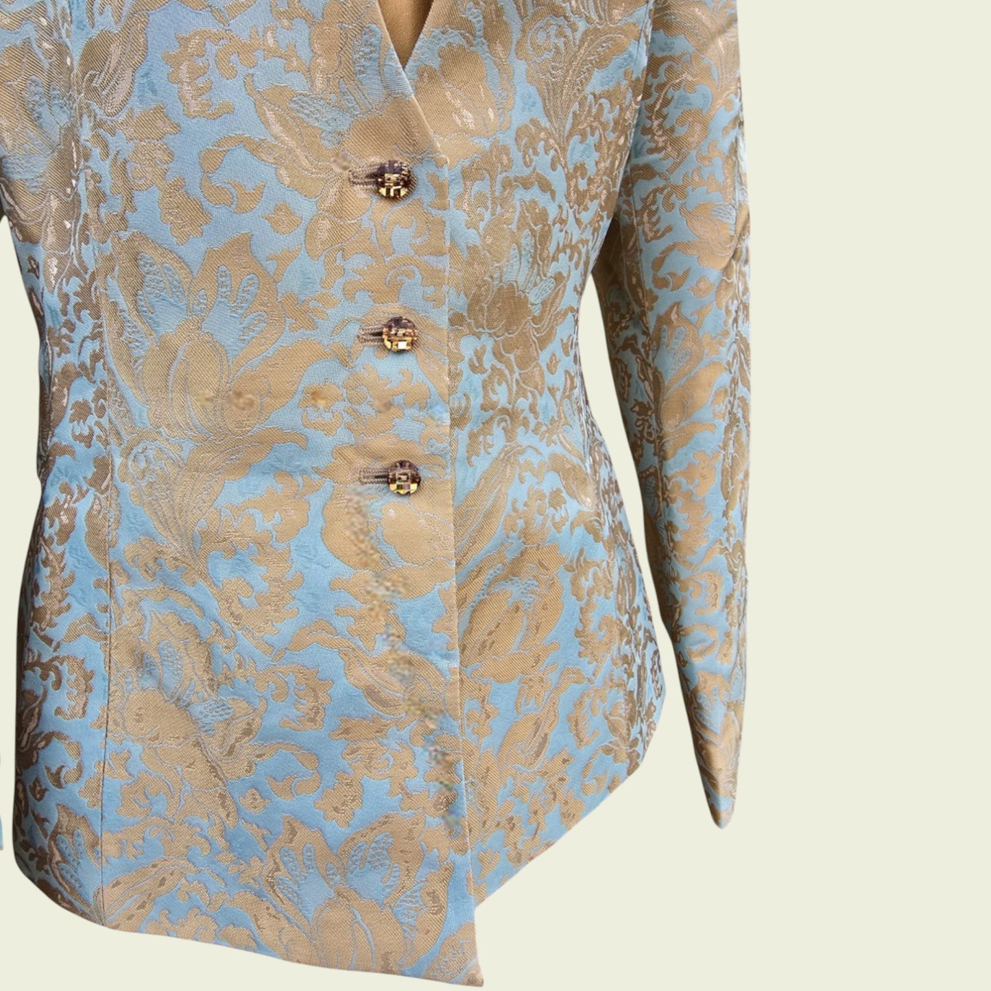 Light blue and gold jacket with button detail on a beige background