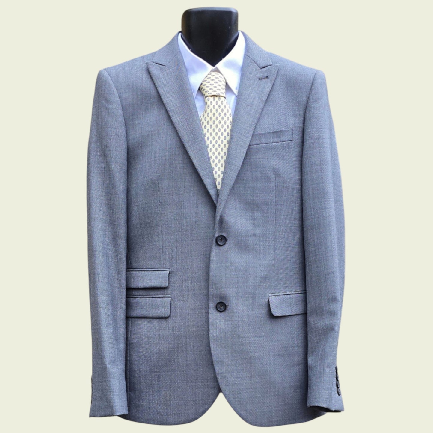 Gray suit jacket with a white shirt and patterned tie on a mannequin against a beige background