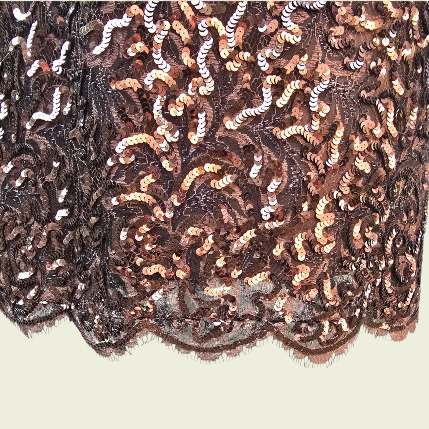 Close-up of sequined dress hemline with gold and black pattern on a beige background