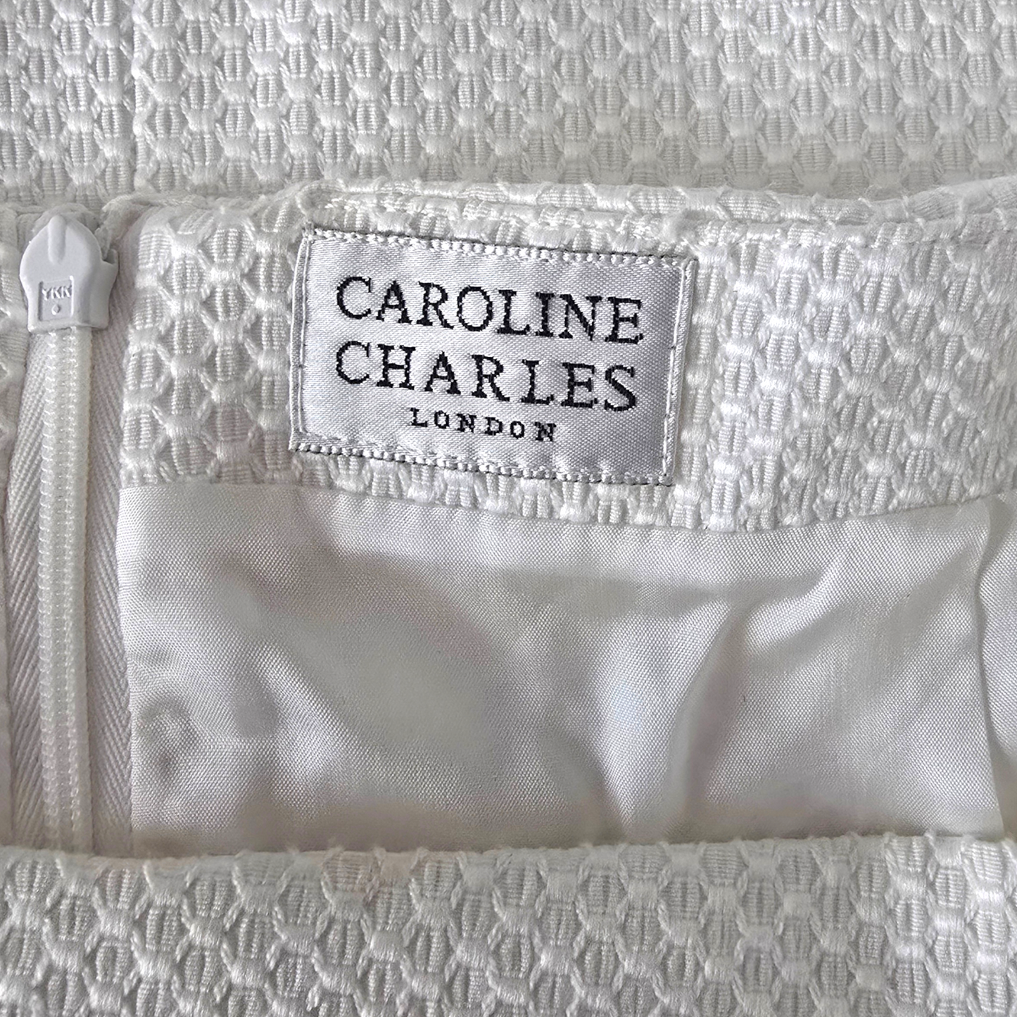 Close-up of a white textured fabric with 'Caroline Charles London' label.