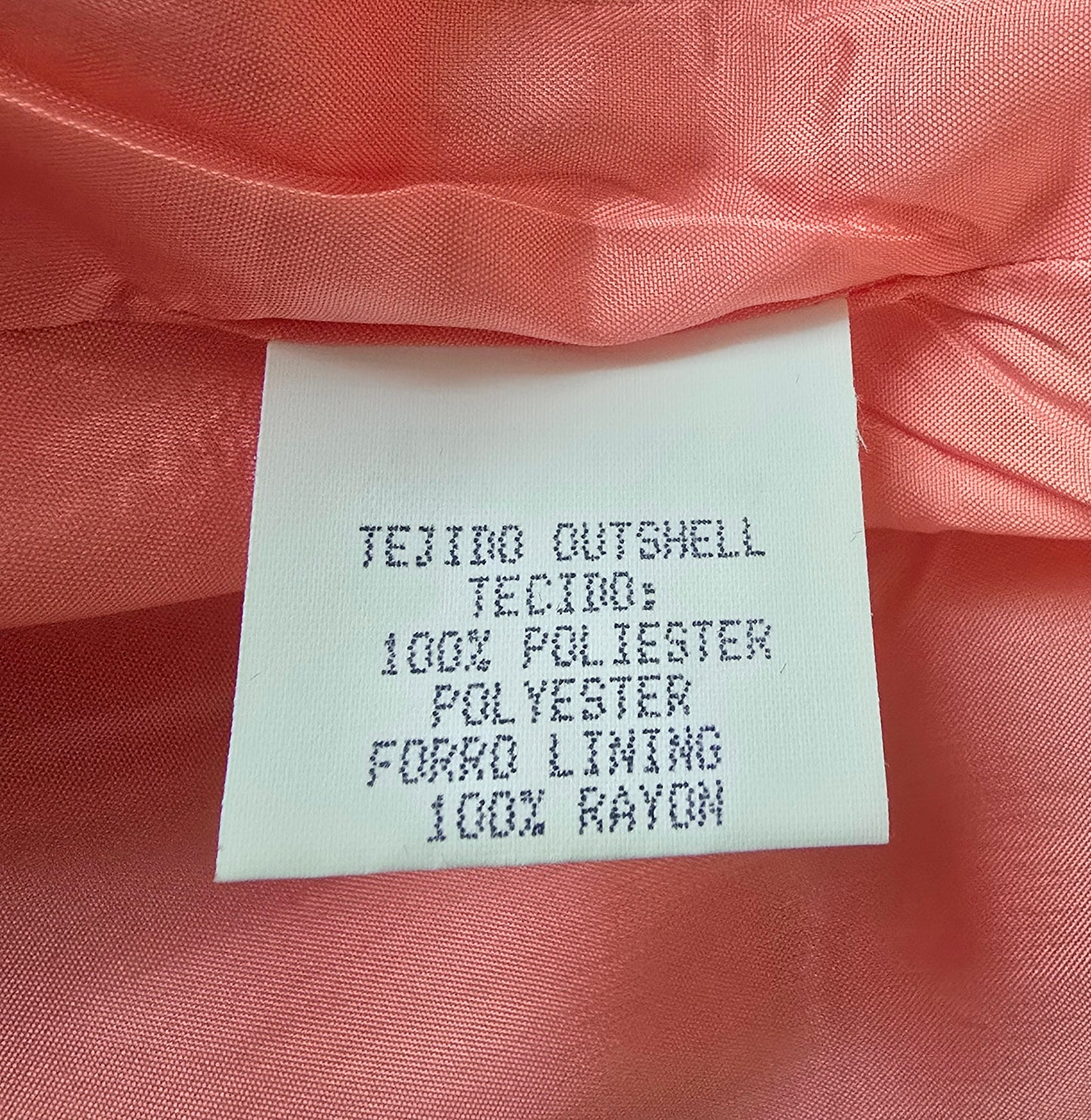 Fabric label on a pink fabric background with text about material composition.