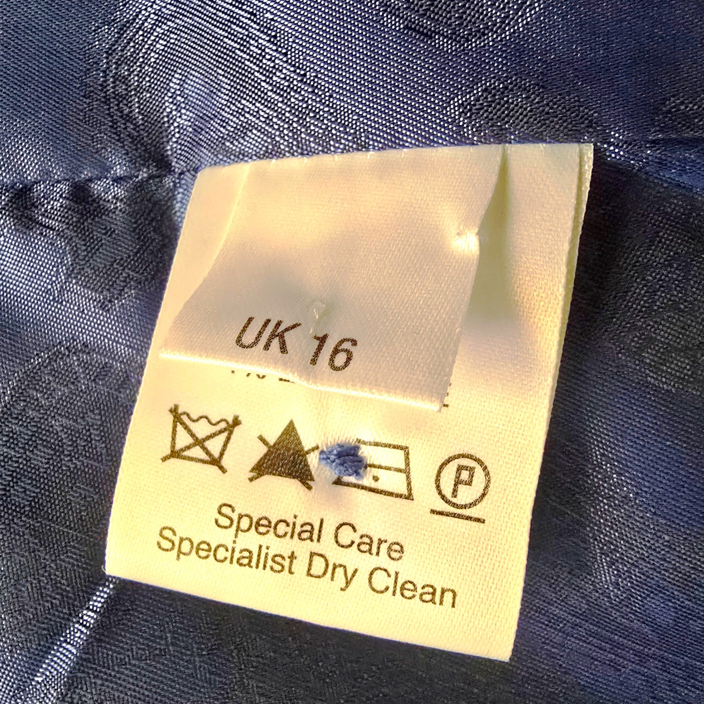Clothing label with size 'UK 16' and care instructions on a blue fabric background