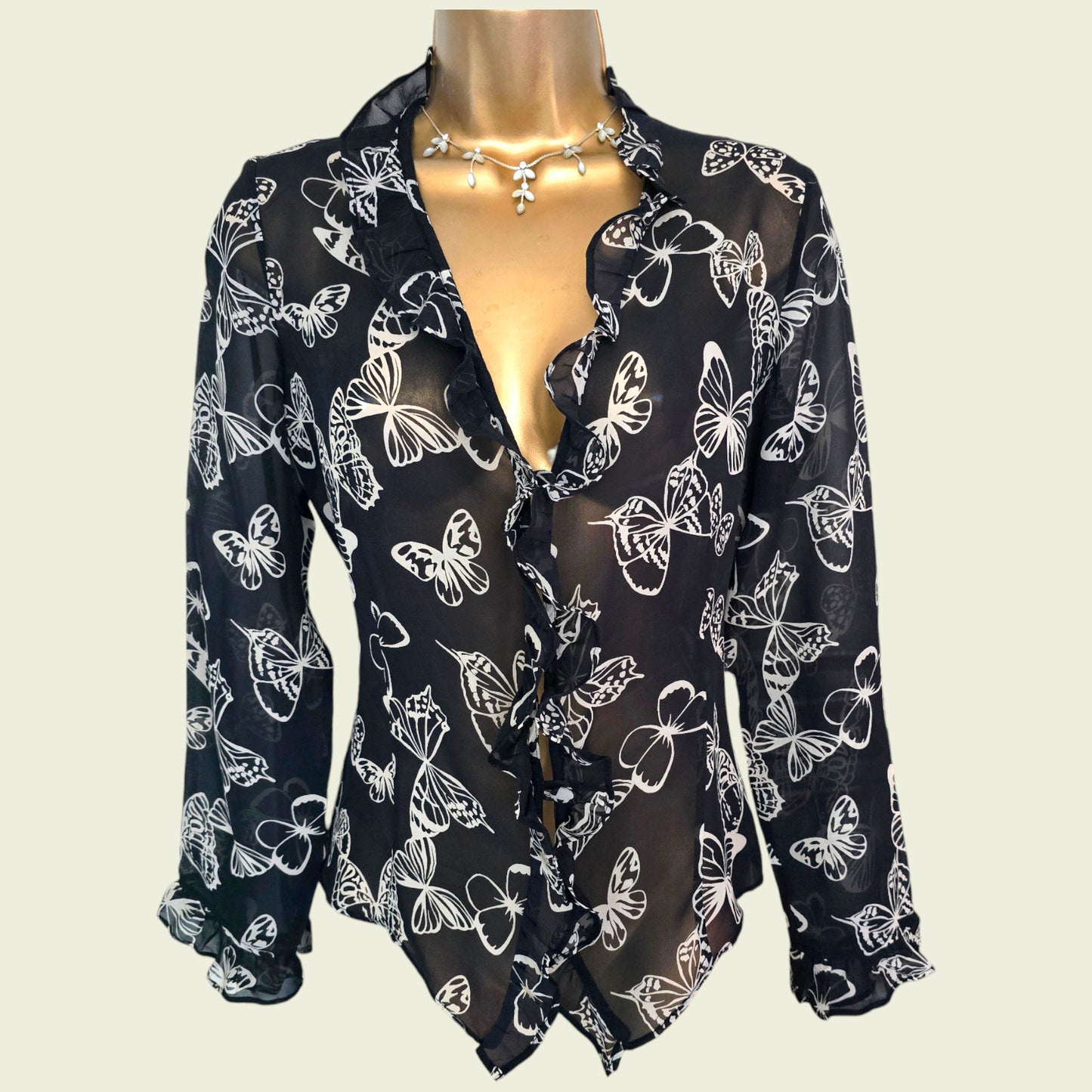 Black blouse with white butterfly patterns on a mannequin against a plain background