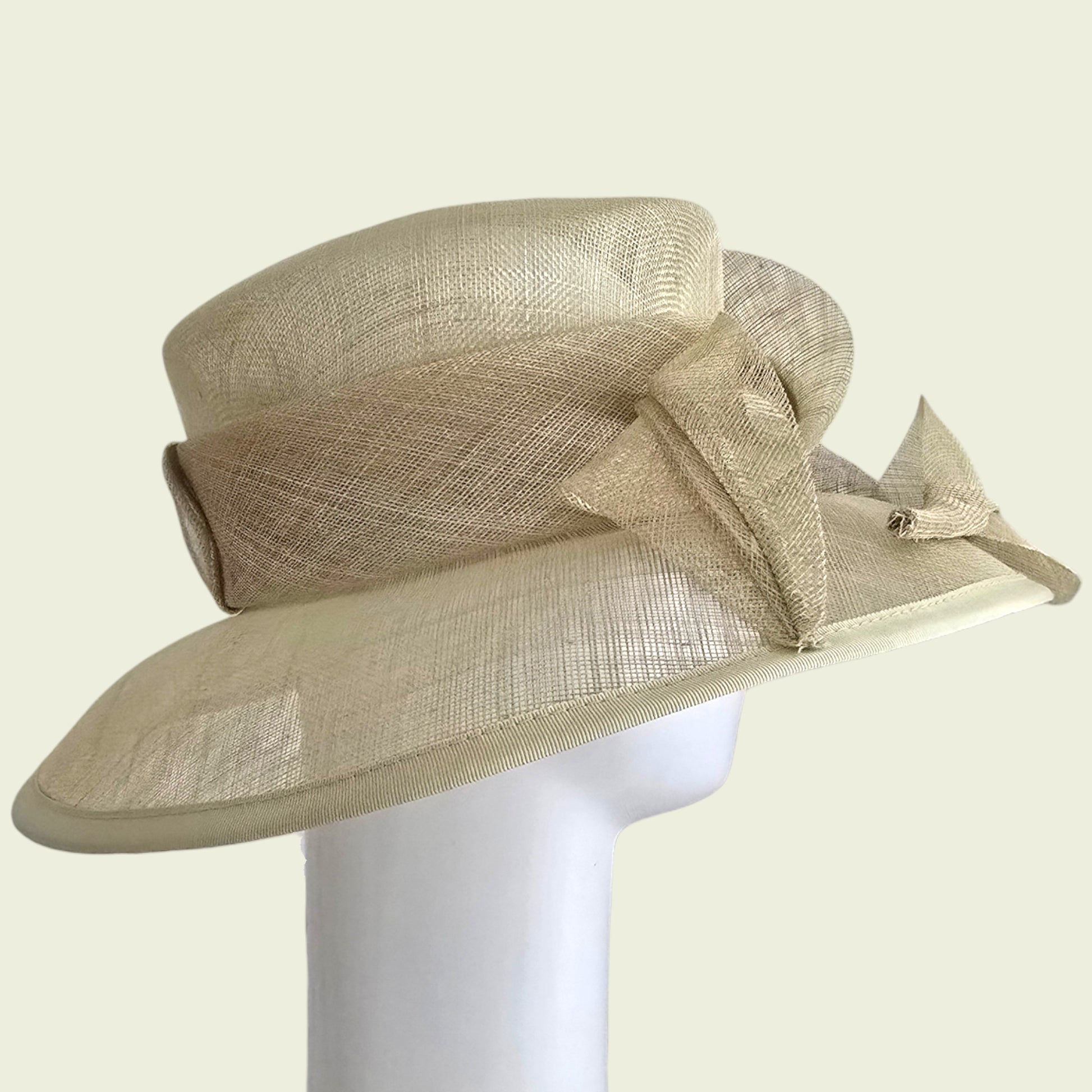 Beige straw hat with a large bow on a white stand against a beige background