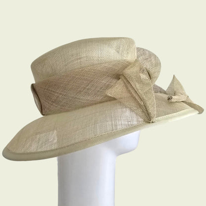 Beige straw hat with a large bow on a white stand against a beige background