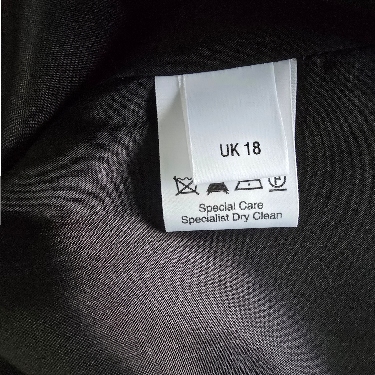 Clothing label on a dark fabric background with text and symbols.