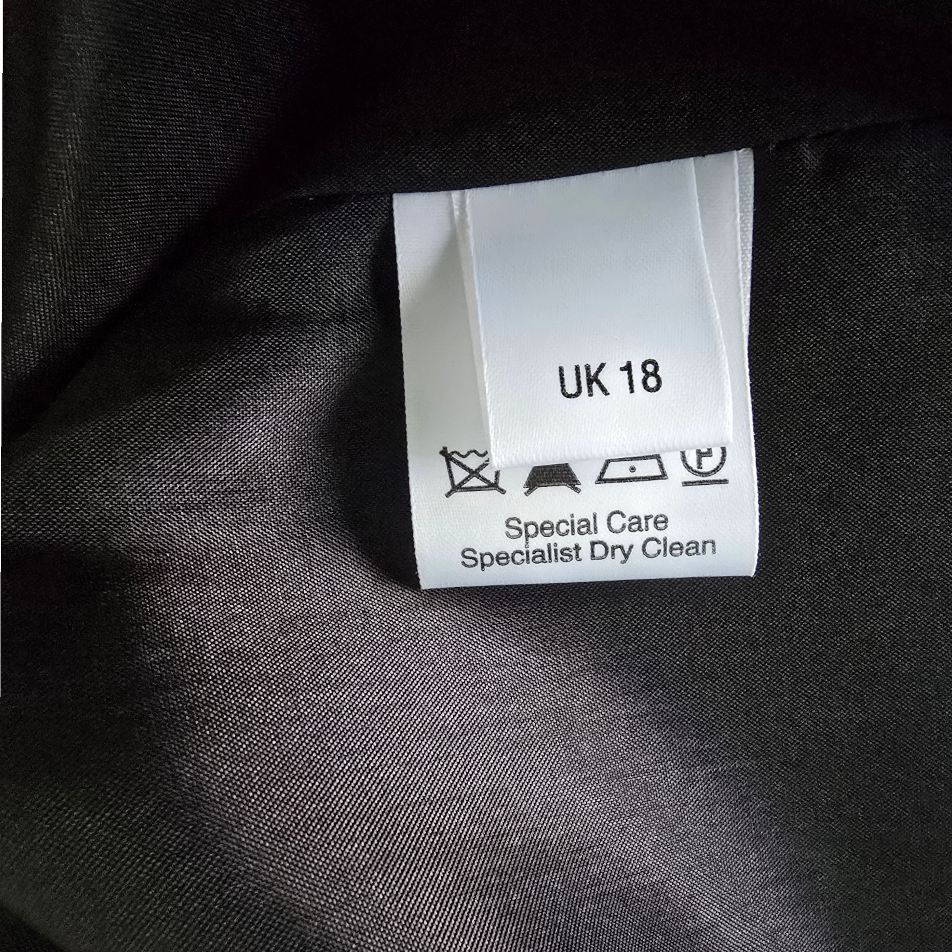 Clothing label on a dark fabric background with text and symbols.