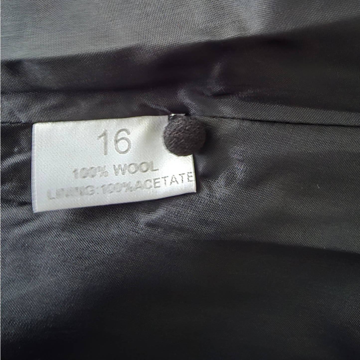 Clothing label on a gray fabric background with '16' and material details.