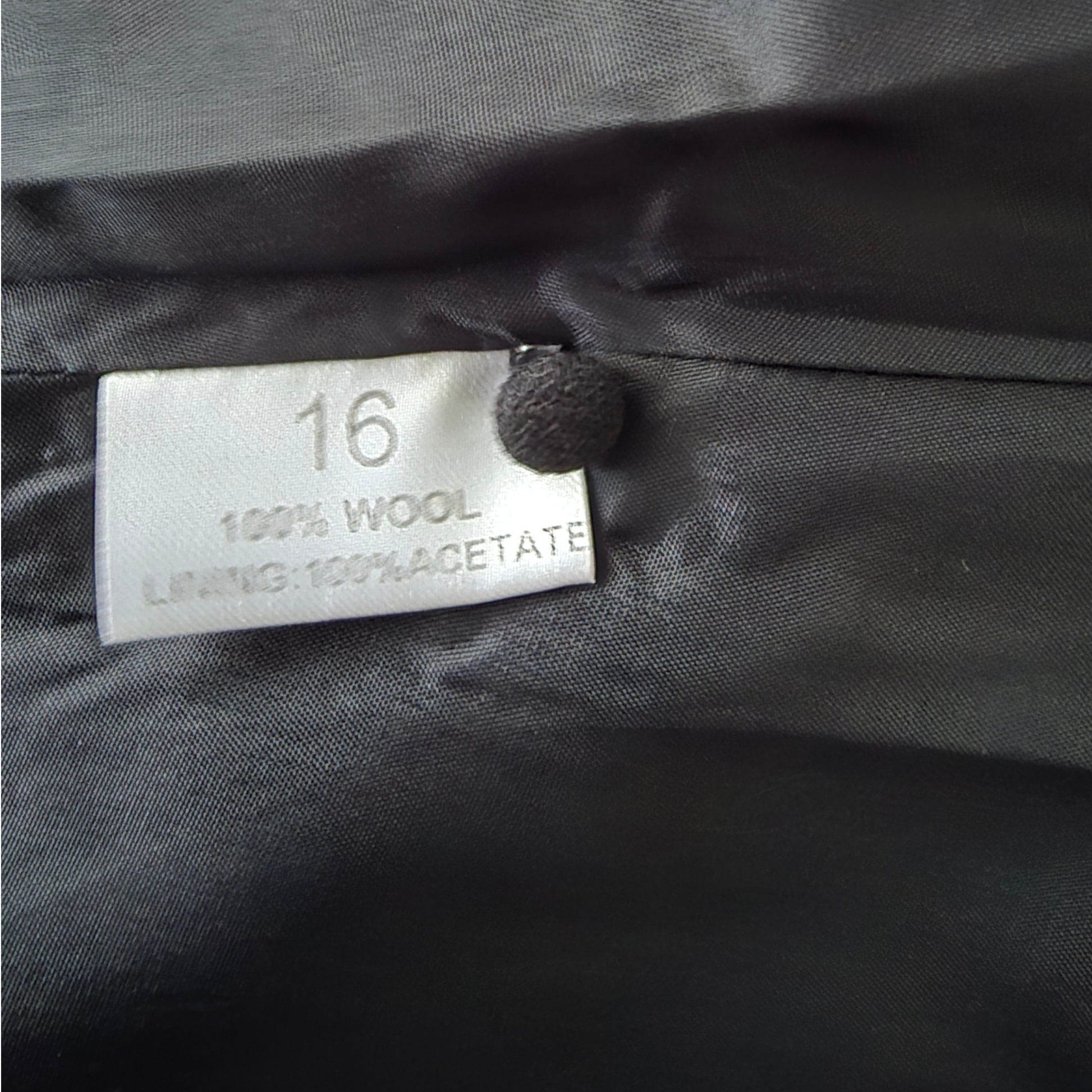 Clothing label on a gray fabric background with '16' and material details.