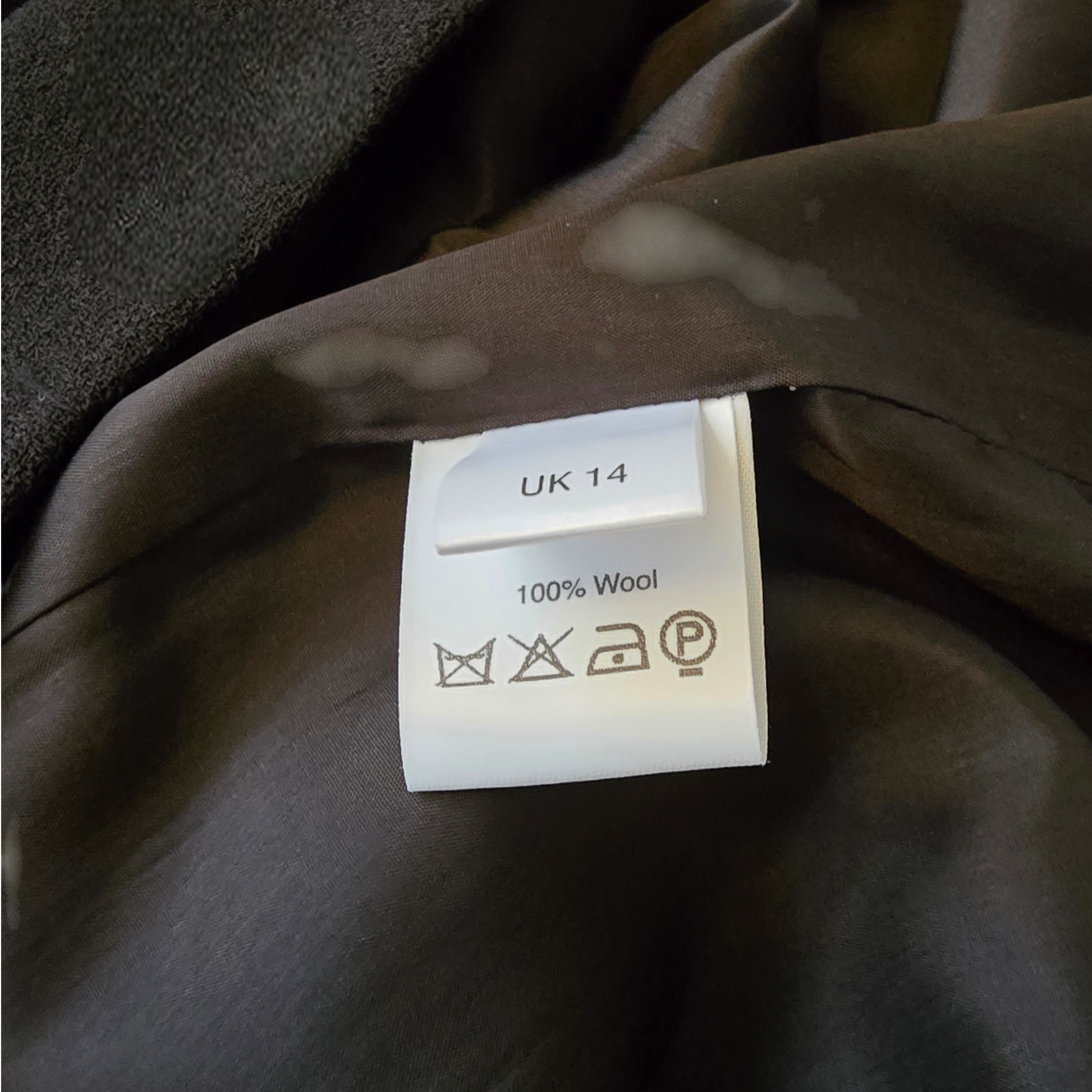 Clothing label on a brown garment with size 'UK 14' and material '100% Wool'.
