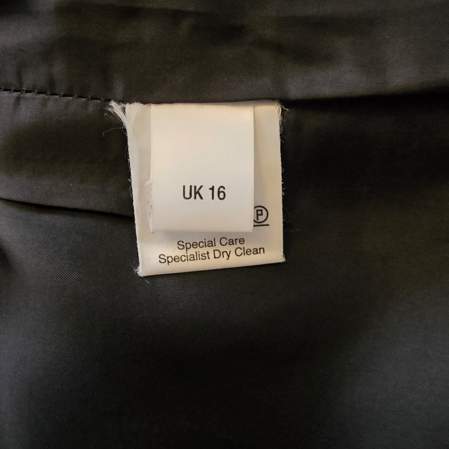Clothing label on a black garment with size 'UK 16' and care instructions.
